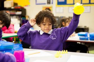 Student raising yellow cup to uncover multiple yellow teddy bears for math problem.