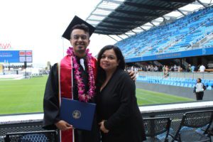 Noel and his mother Lourdes at this SJSU graduation. Photo taken at a sports stadium, both he and her are in the front row with field shown behind them.