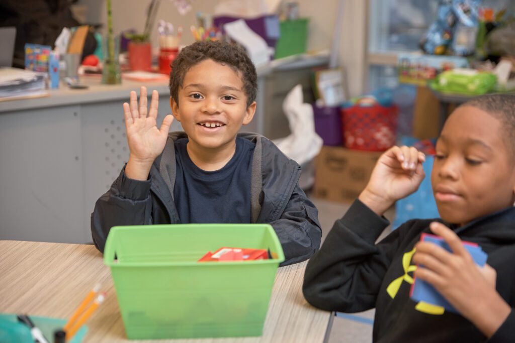 young student waves to camera while in class